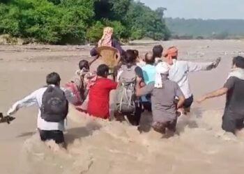 बहती ताल नदी की तेज धारा में कुर्सी में बीमार को जान जोखिम में डालकर लेकर जाते स्थानीय निवासी